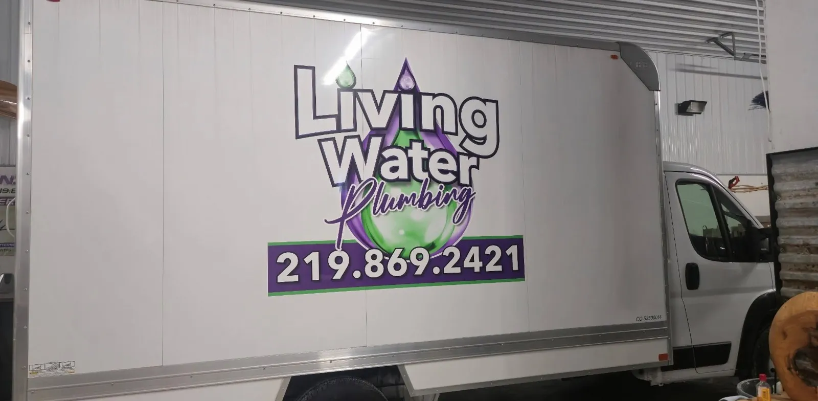Side of the Living Water Plumbing box truck showing the purple and green water-drop logo and the phone number 219.869.2421